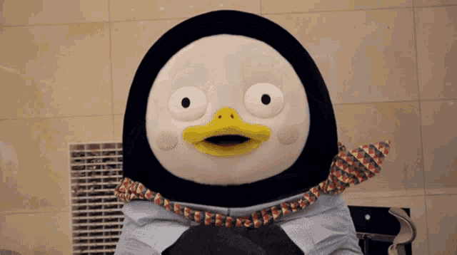 a stuffed penguin with a yellow beak is holding a cat