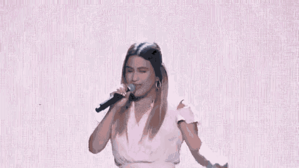 a woman in a pink dress is standing on a stage holding a microphone .