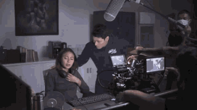 a man in a blue hoodie with the word life on it stands behind a woman sitting at a desk