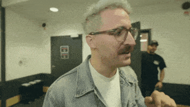 a man with glasses and a mustache stands in a room