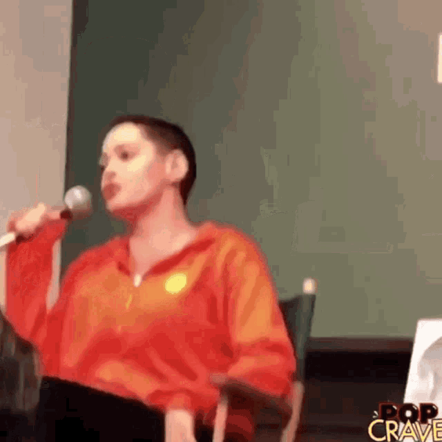 a woman is sitting in a chair holding a microphone and talking into it .