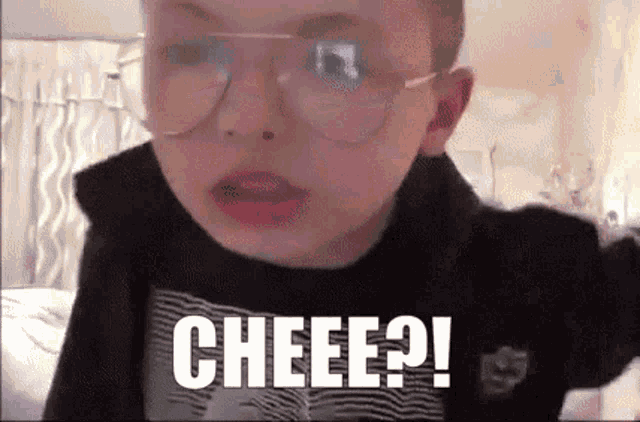 a young boy wearing glasses and a black shirt is making a funny face and saying cheee .