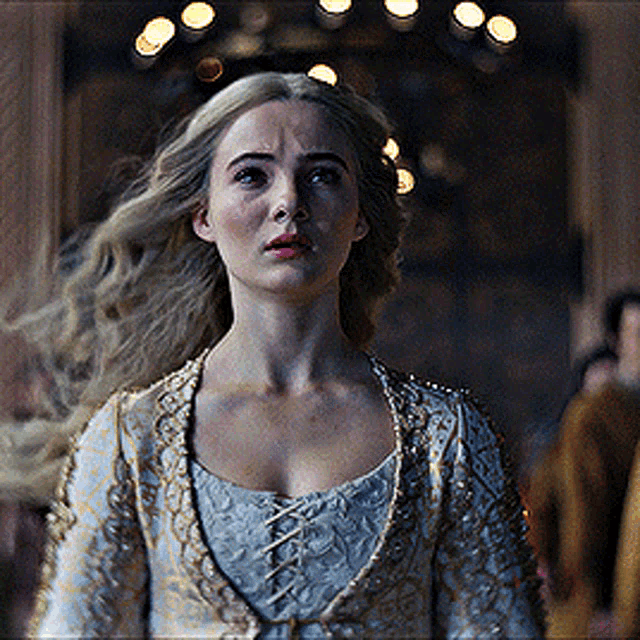 a woman with long blonde hair is wearing a gold and white dress .