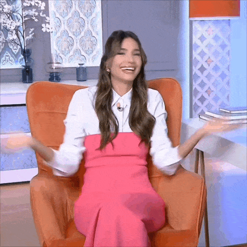 a woman in a pink dress is sitting in an orange chair