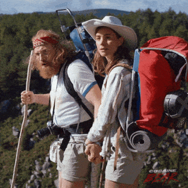 a man and a woman with backpacks are holding hands on top of a hill