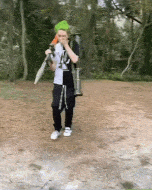a person wearing a green hat and holding an umbrella is walking in the woods .
