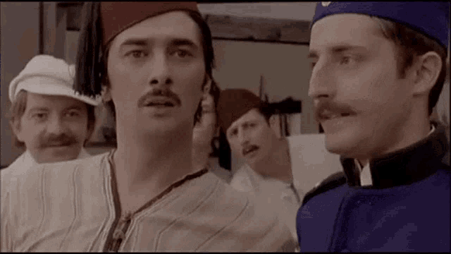 a group of men with mustaches and hats are standing next to each other and talking .