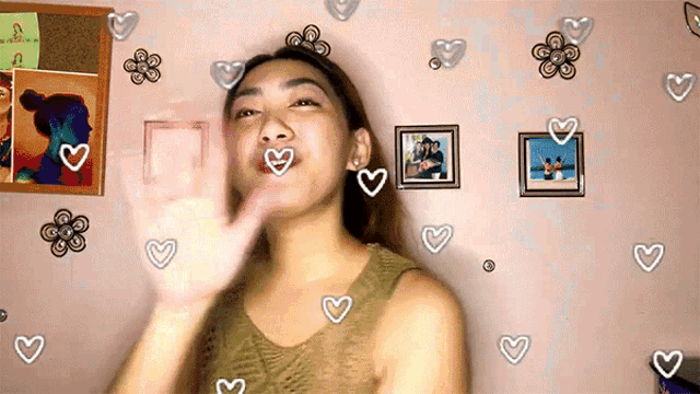 a woman is waving her hand in front of a wall with hearts and flowers on it