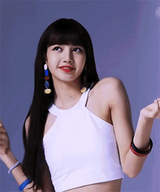 a woman with long black hair is wearing a white crop top and colorful earrings .