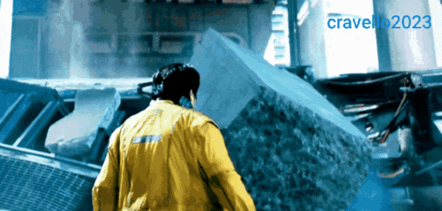 a man in a yellow jacket stands in front of a large rock and the year 2023 is visible