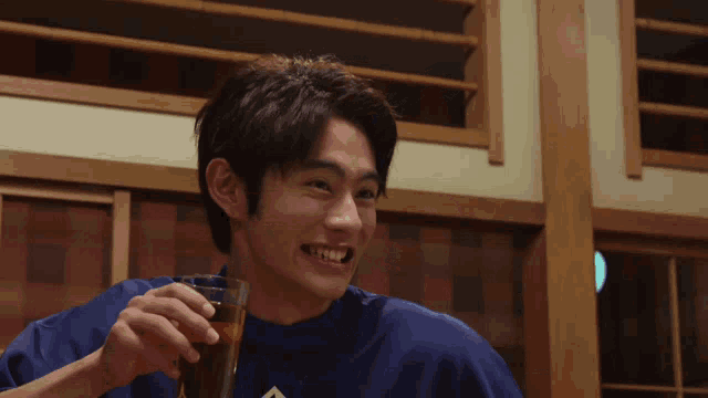 a man in a blue shirt is smiling and holding a drink