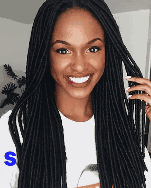 a woman with dreadlocks is wearing a white shirt with the letter s on the sleeve