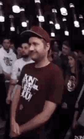 a man wearing a hat and a maroon t-shirt is standing in front of a crowd .