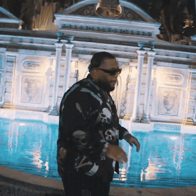 a man wearing sunglasses and a skull and crossbones shirt stands in front of a pool