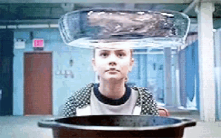 a woman is sitting in front of a pot of water with a glass bowl on her head .