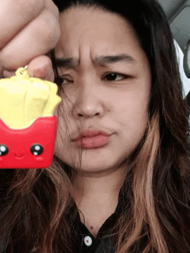 a woman is holding a red and yellow french fries keychain