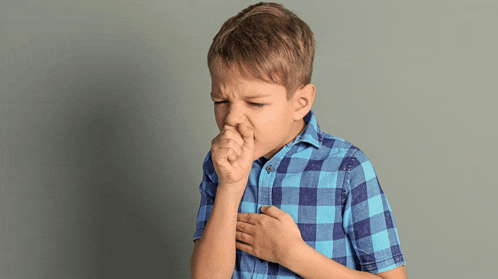 a young boy in a blue plaid shirt is coughing into his hand