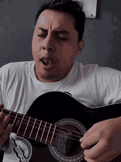 a man in a white shirt is singing while playing an acoustic guitar