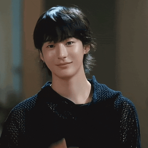 a young man wearing a black shirt and earrings smiles