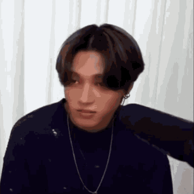 a young man wearing a turtleneck sweater and a necklace is sitting in front of a white curtain .