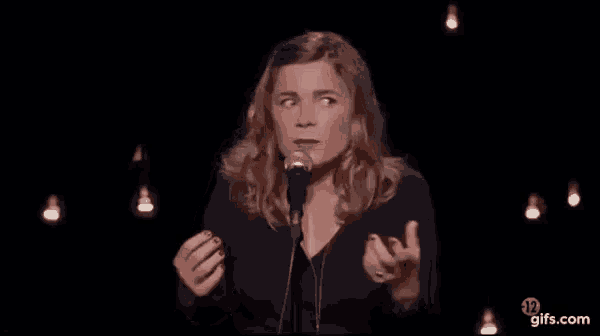 a woman is standing in front of a microphone on a stage and making a funny face .
