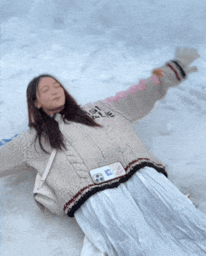a woman laying in the snow with her arms outstretched wearing a sweater that says chanel