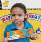 a little girl in a blue shirt is holding a sign that says " student of the week "