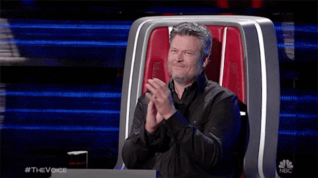 a man sits in a chair with his hands folded in front of a screen that says the voice