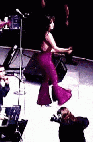 a woman in a purple jumpsuit is dancing on a stage while a man takes a picture .
