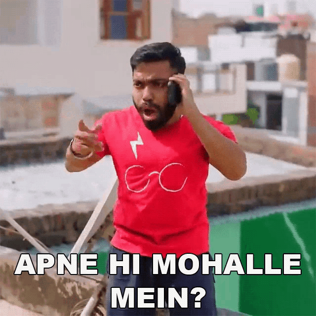 a man in a red shirt is talking on a cell phone and has the words apne hi mohalle mein written below him