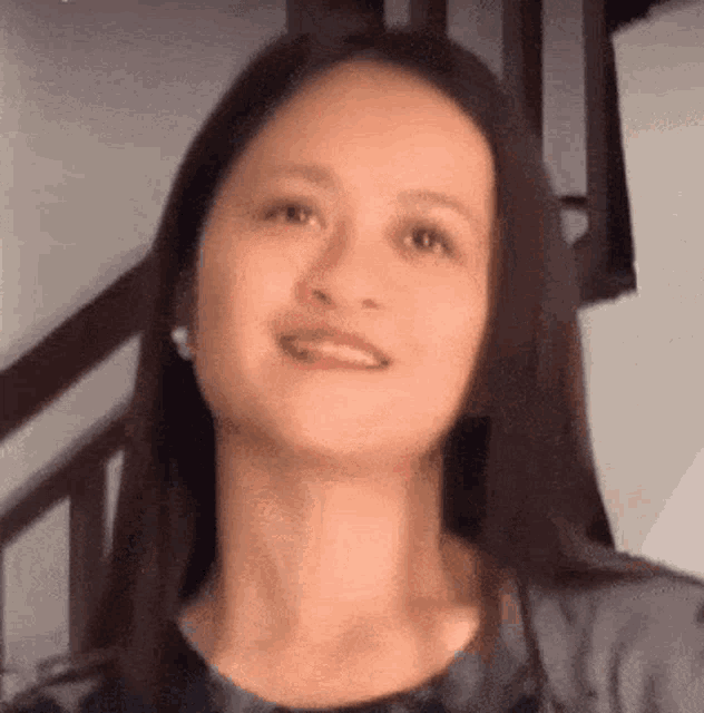 a woman with long dark hair is smiling in front of a staircase