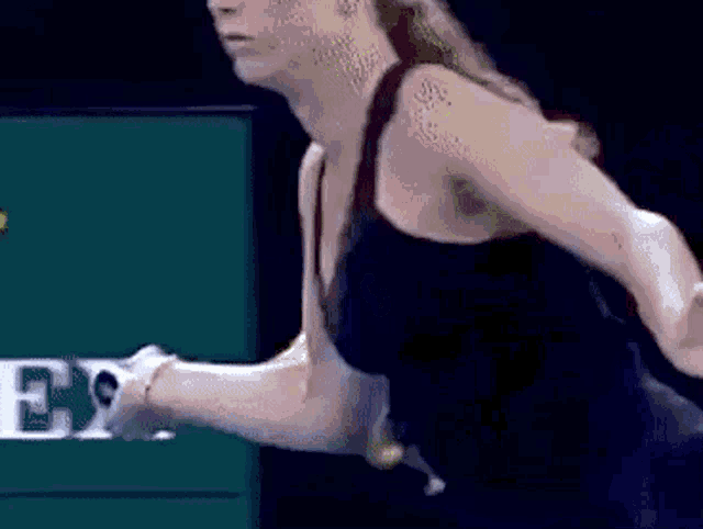 a woman in a black tank top is holding a tennis racket in her hand .