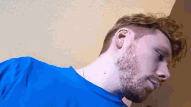 a man with a beard wearing a blue shirt looks down