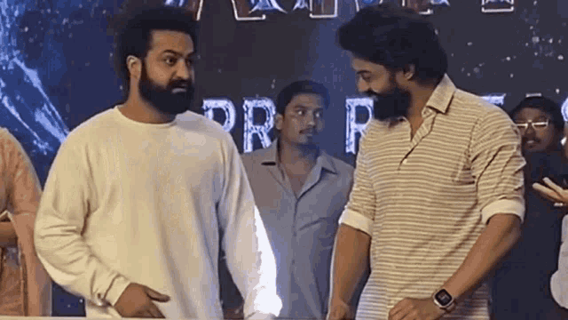 two men with beards are standing next to each other in front of a crowd of people .
