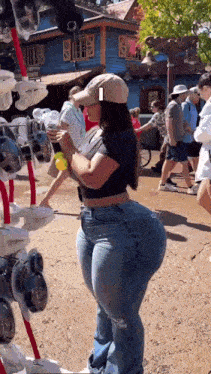a woman wearing a hat and jeans is standing in a crowded area holding a yellow ball .