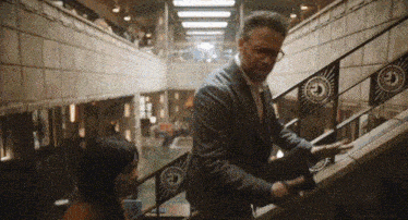 a man in a suit and tie is walking down a set of stairs with the letter e on the railing