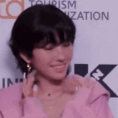 a woman wearing a pink sweater and earrings is smiling and looking at the camera .