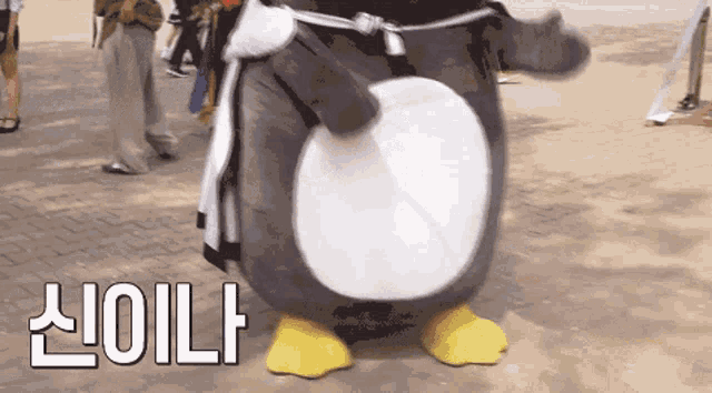 a penguin mascot is standing on a brick sidewalk with the words " oil " written above it