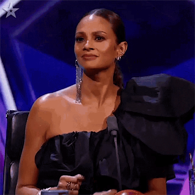 a woman in a black dress and earrings is sitting in front of a microphone .