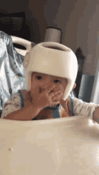 a baby wearing a helmet is covering his nose with his hand