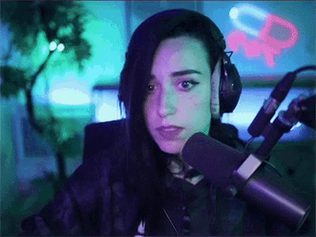 a woman wearing headphones stands in front of a microphone with a neon sign in the background