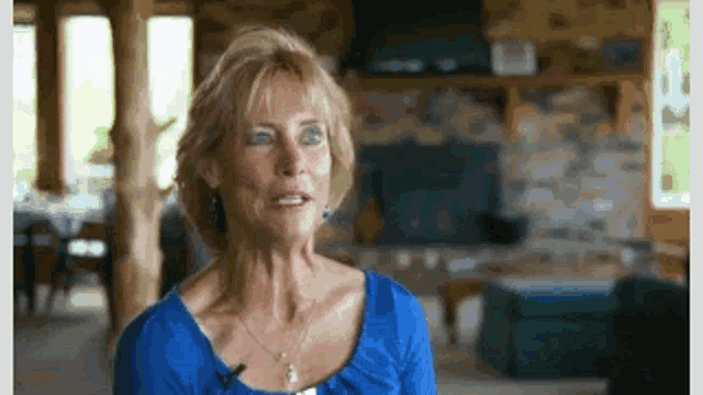 a woman in a blue shirt is sitting in a living room with a microphone .