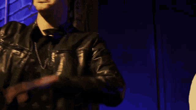 a man wearing a black beanie and a leather jacket is making a stop sign with his hands