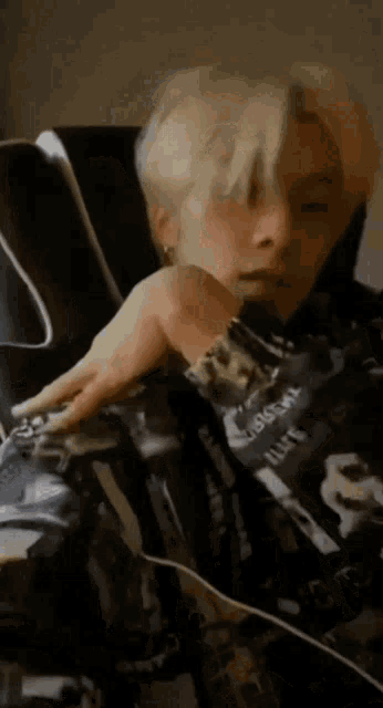 a man with blonde hair is sitting in a chair with his hand on his shoulder .