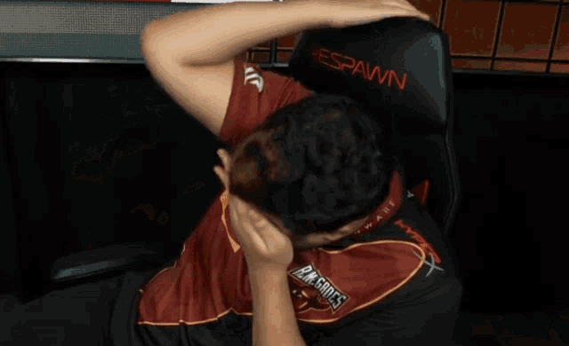 a man in a spawn gaming chair covering his face with his hands