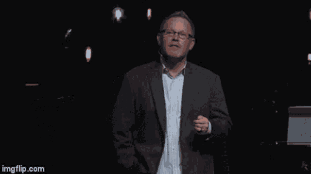 a man in a suit and glasses is dancing on a stage with imgflip.com in the corner