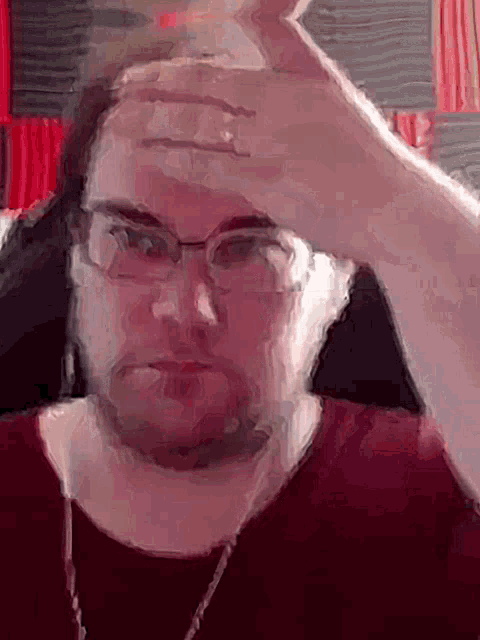a man wearing glasses and a red shirt has his hand on his head