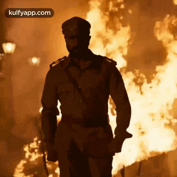 a man in a police uniform is standing in front of a large fire .