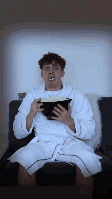 a man sitting on a couch eating a bowl of popcorn