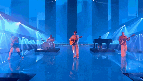 a man is playing a guitar on a stage in front of a drum set .